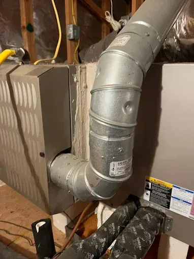 A metal pipe is coming out of a furnace in a basement.