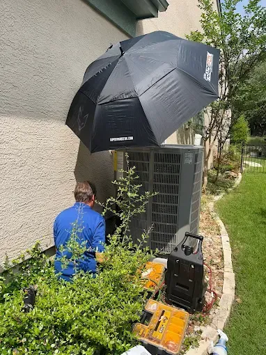 A man is sitting under an umbrella next to an air conditioner.