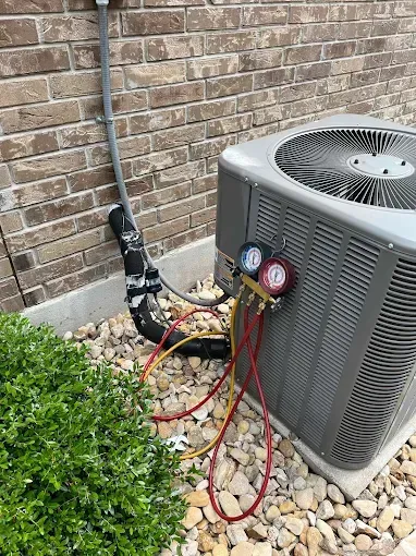 A gray air conditioner is sitting on top of a pile of rocks next to a brick wall.