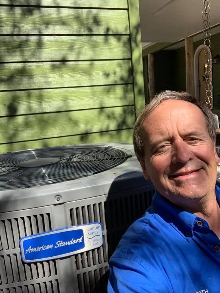 A man in a blue shirt is standing in front of an air conditioner.