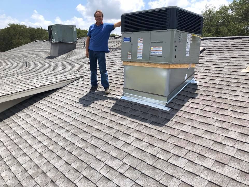 A man is standing on top of a roof next to a large air conditioner.