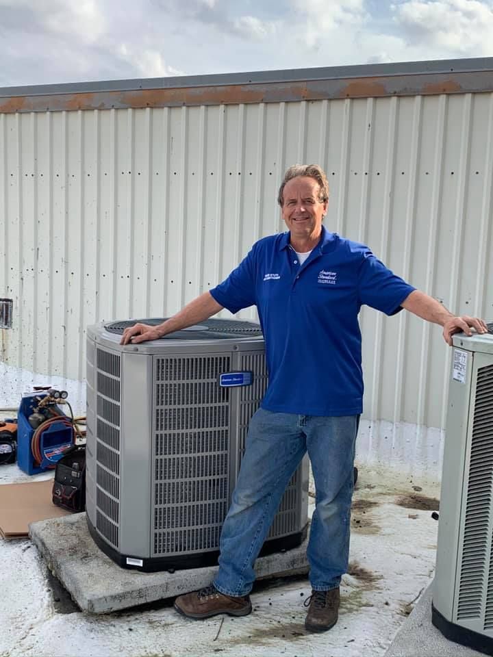 A man in a blue shirt is standing next to an air conditioner.