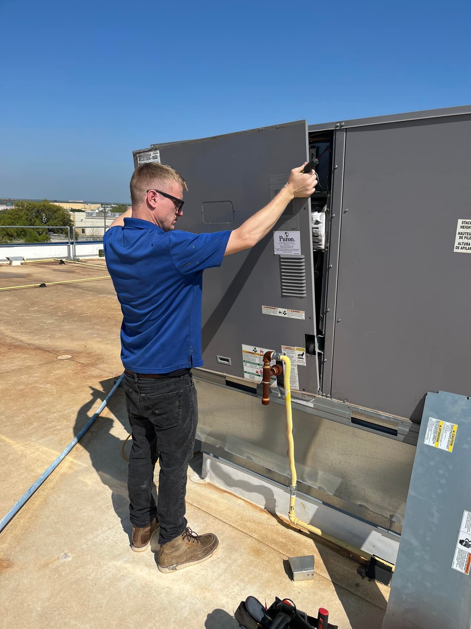 A man is working on a rooftop air conditioner.