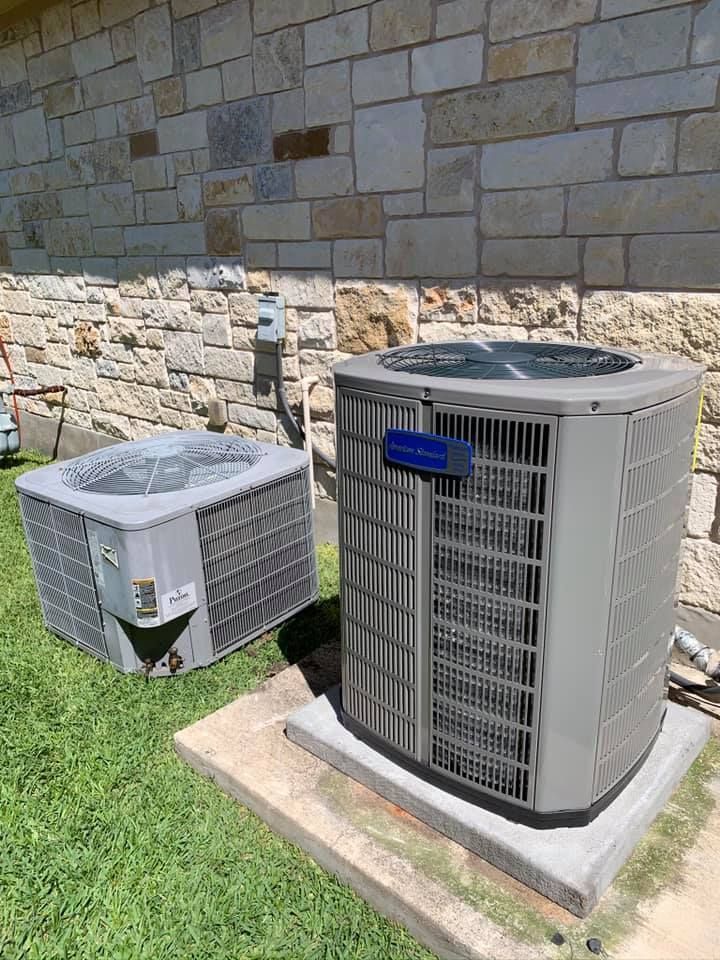Two air conditioners are sitting next to each other in front of a brick wall.
