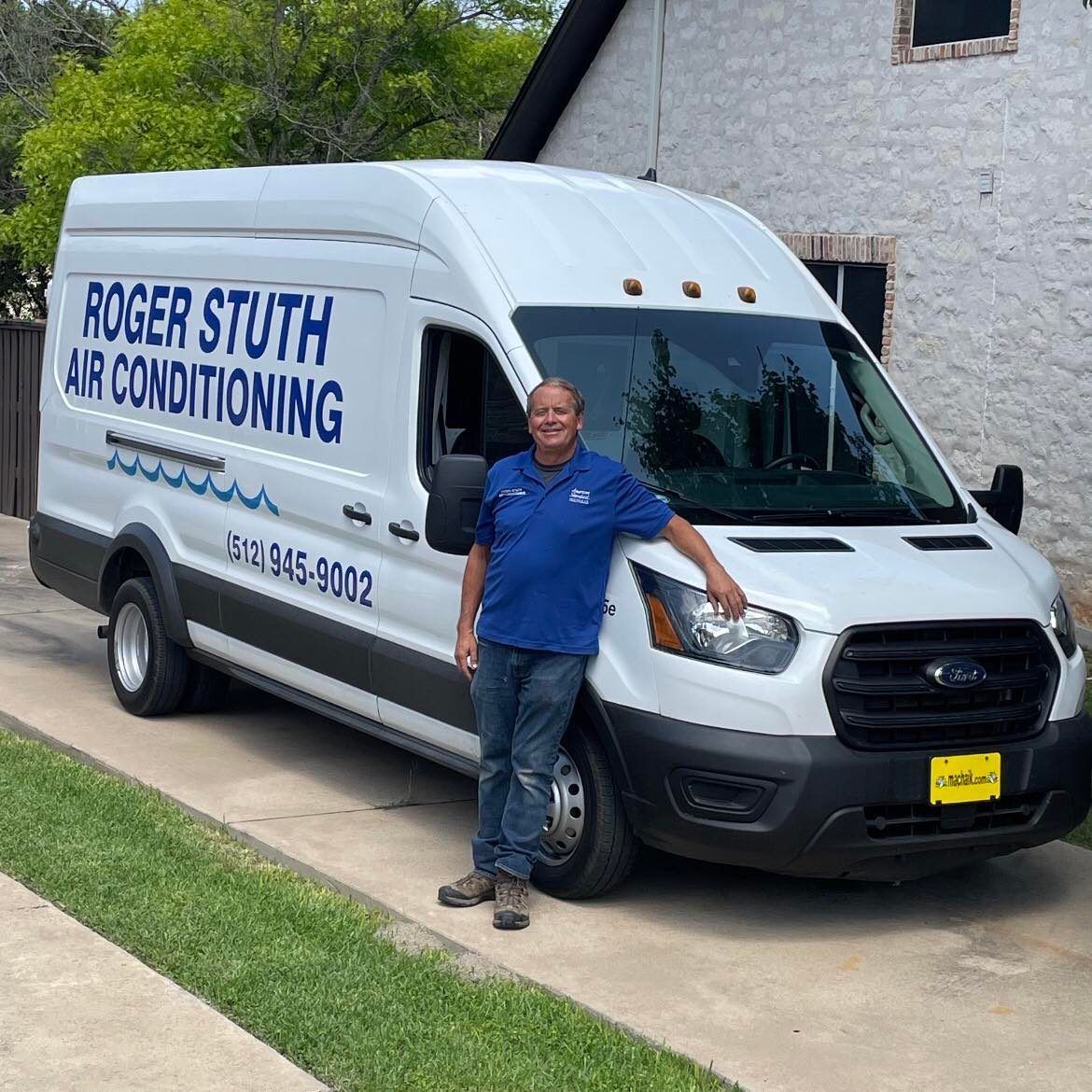 A man is standing in front of a roger stuth air conditioning van.