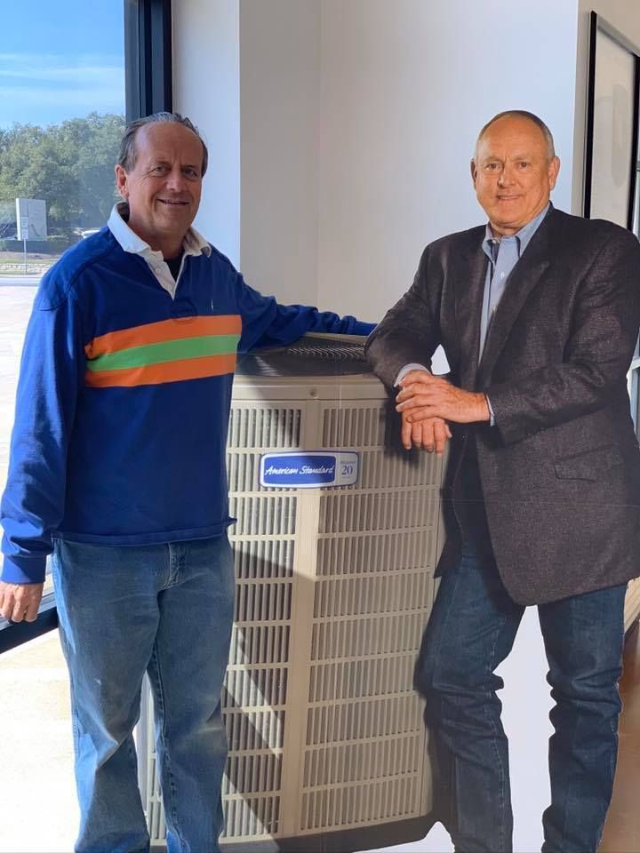 Two men standing next to each other in front of an air conditioner