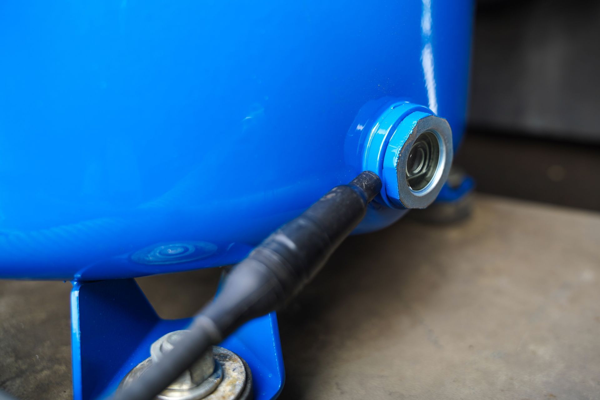 Blue air compressor tank with a metal fitting and attached black wire.