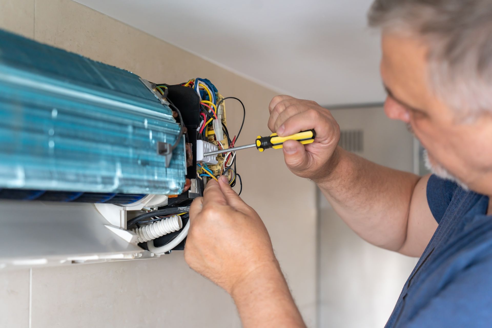Person using a screwdriver to repair a wall-mounted air conditioning unit.