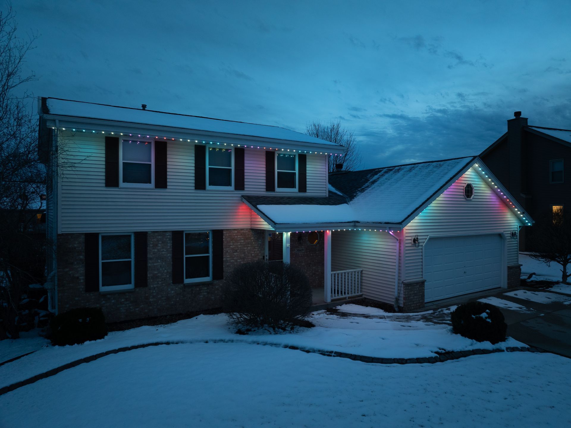 A modern house with christmas lights on it is covered in snow