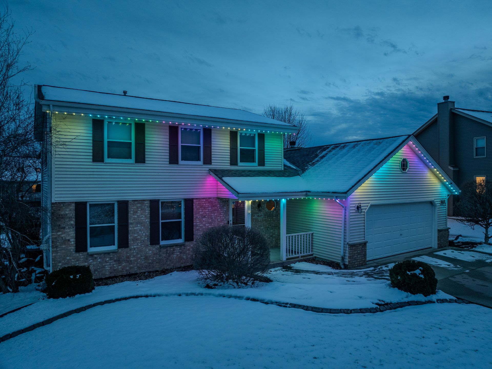 A antique house with Christmas lights on it is covered in snow.