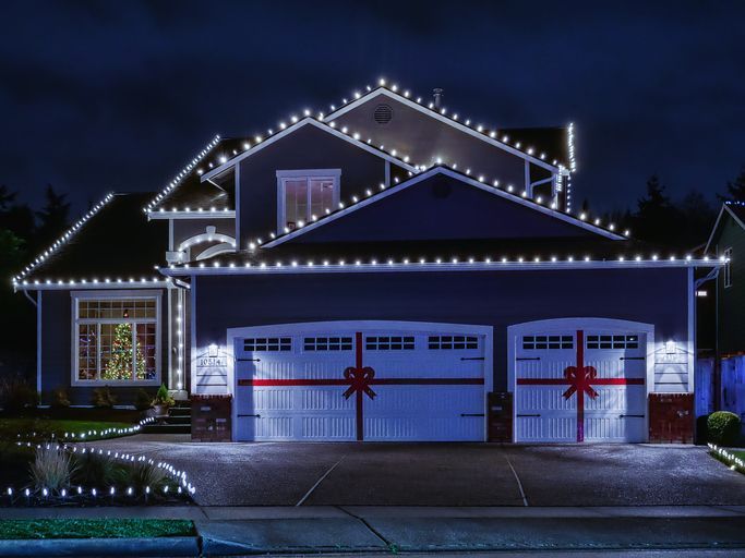 White permanent roofline lighting outlines the roof and garage of a festive house.
