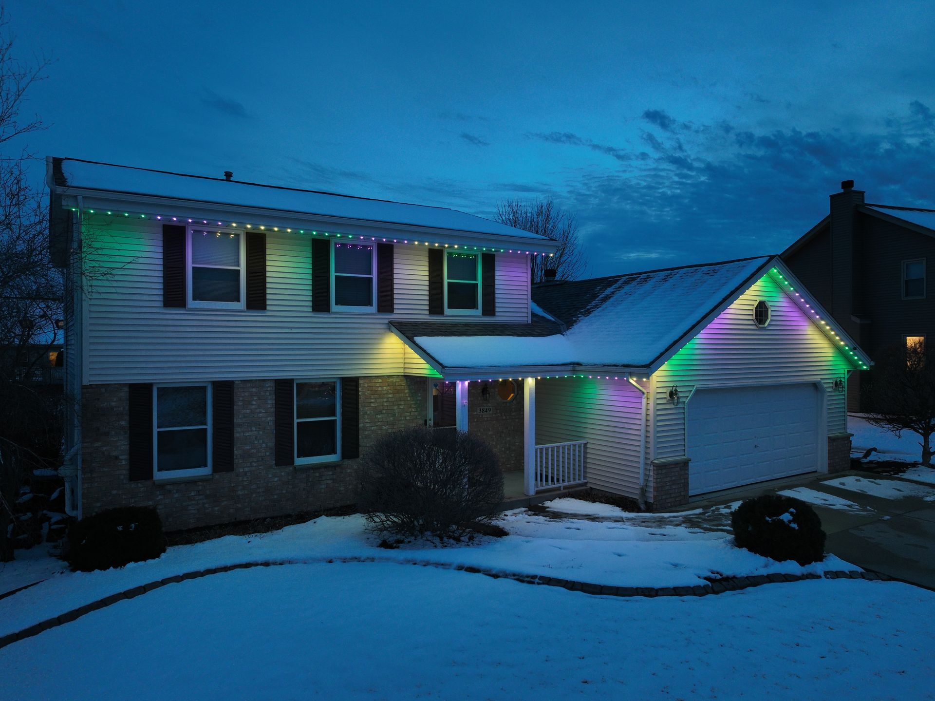 A house with MardiGras thematic lights on it is covered in snow