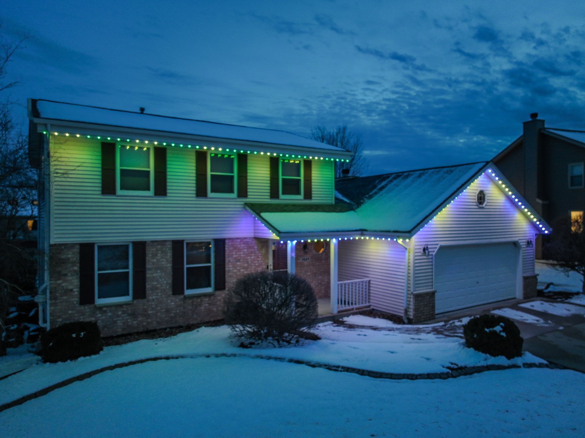 A house with christmas lights on it is covered in snow.