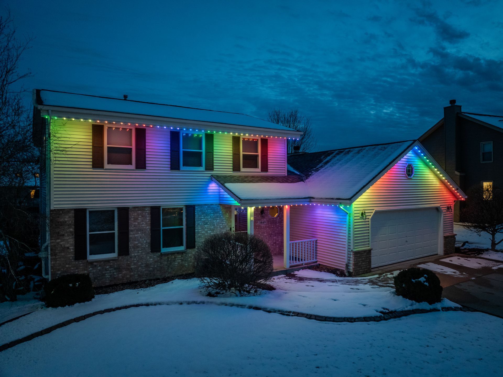 A house with rainbow lights on it is covered in snow.