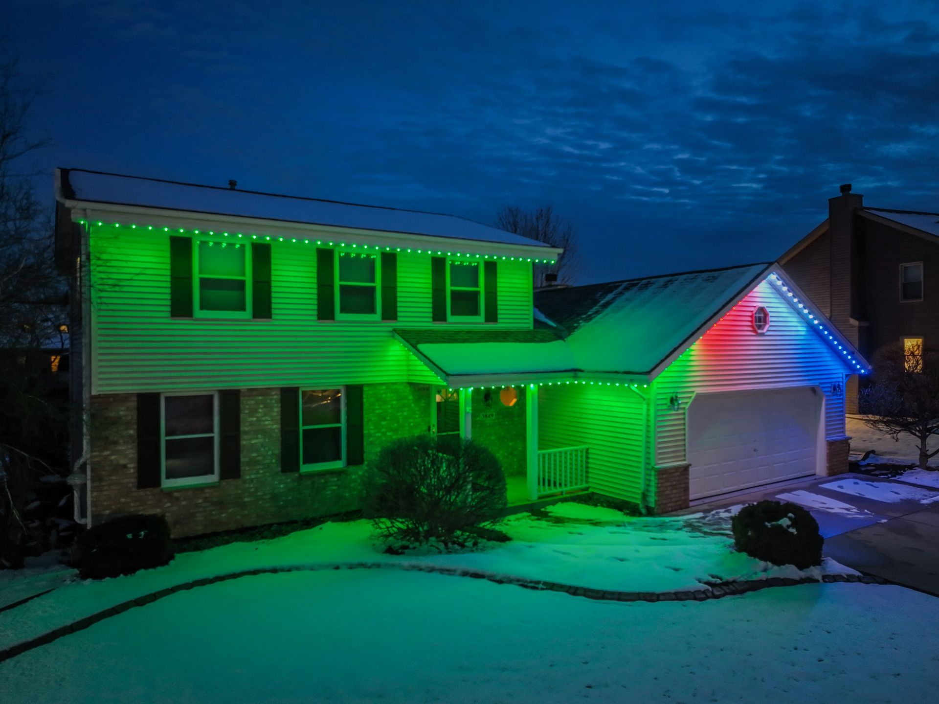 A house with green and Christmas lights on it is covered in snow.
