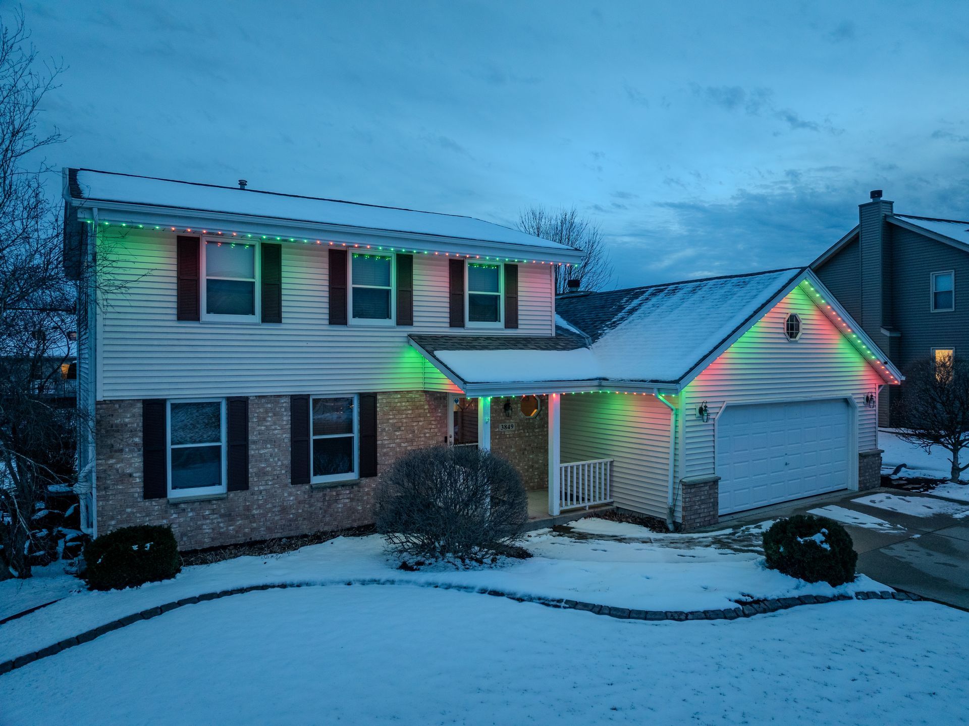 A house with beautiful christmas lights on it is covered in snow
