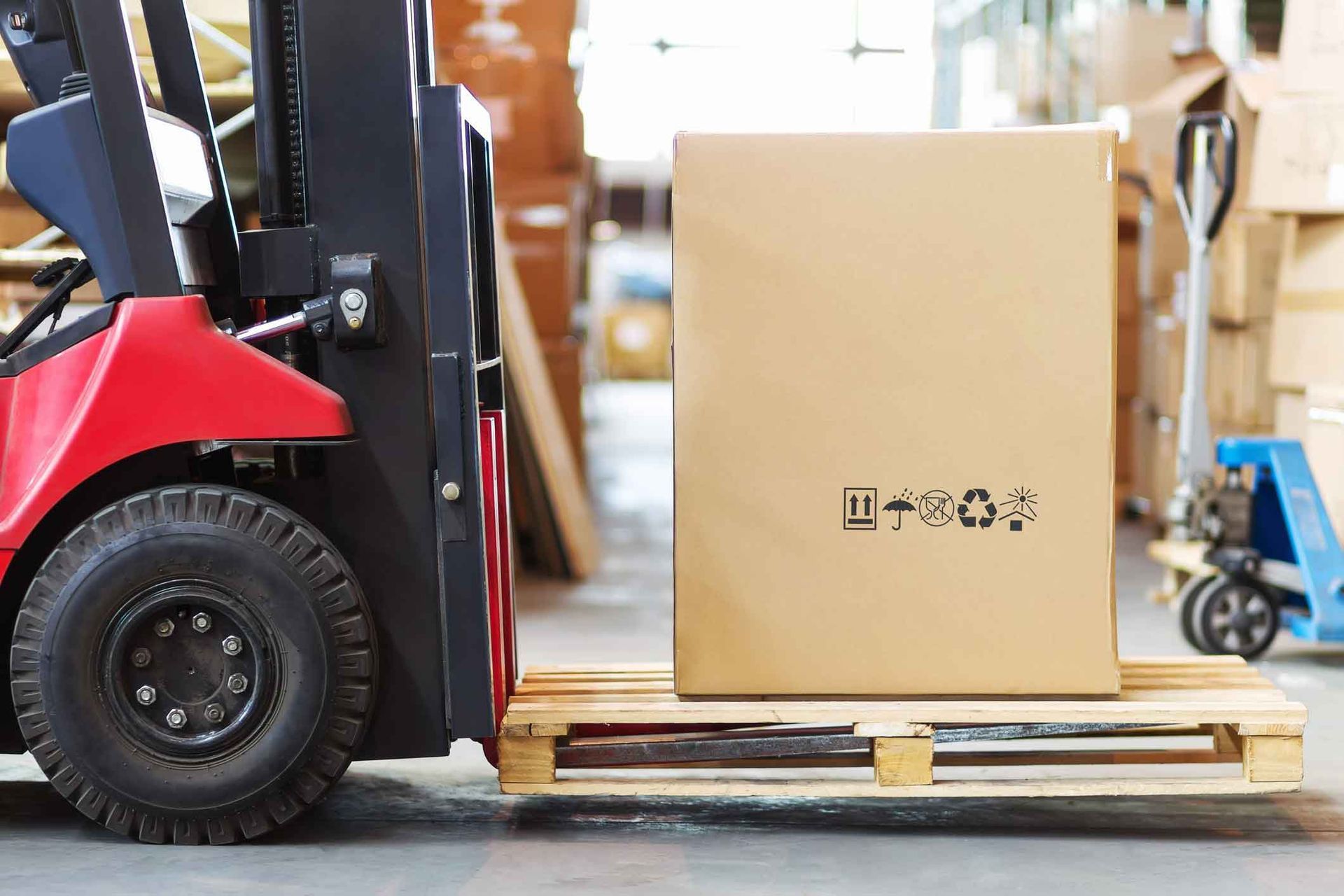A forklift is carrying a cardboard box on a wooden pallet in a warehouse.