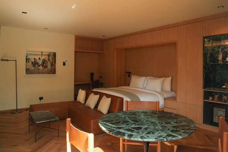 Dormitorio con cama empotrada y escritorio, sofá de cuero marrón, mesa de mármol, paneles de madera y obras de arte.