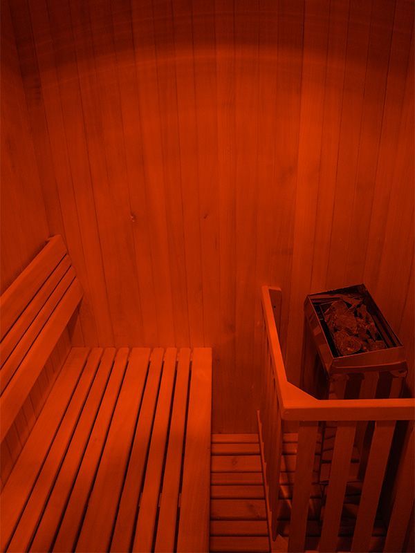 Interior de sauna de madera con banco, calentador e iluminación de color rojo anaranjado.