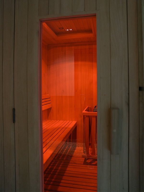 Interior de una sauna, iluminado con un cálido resplandor naranja, bancos de madera y paredes visibles a través de una puerta de vidrio.