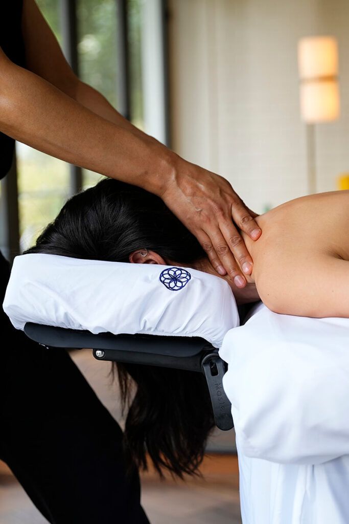 Masajista dando un masaje de cuello a un cliente acostado boca abajo en una mesa de masajes.