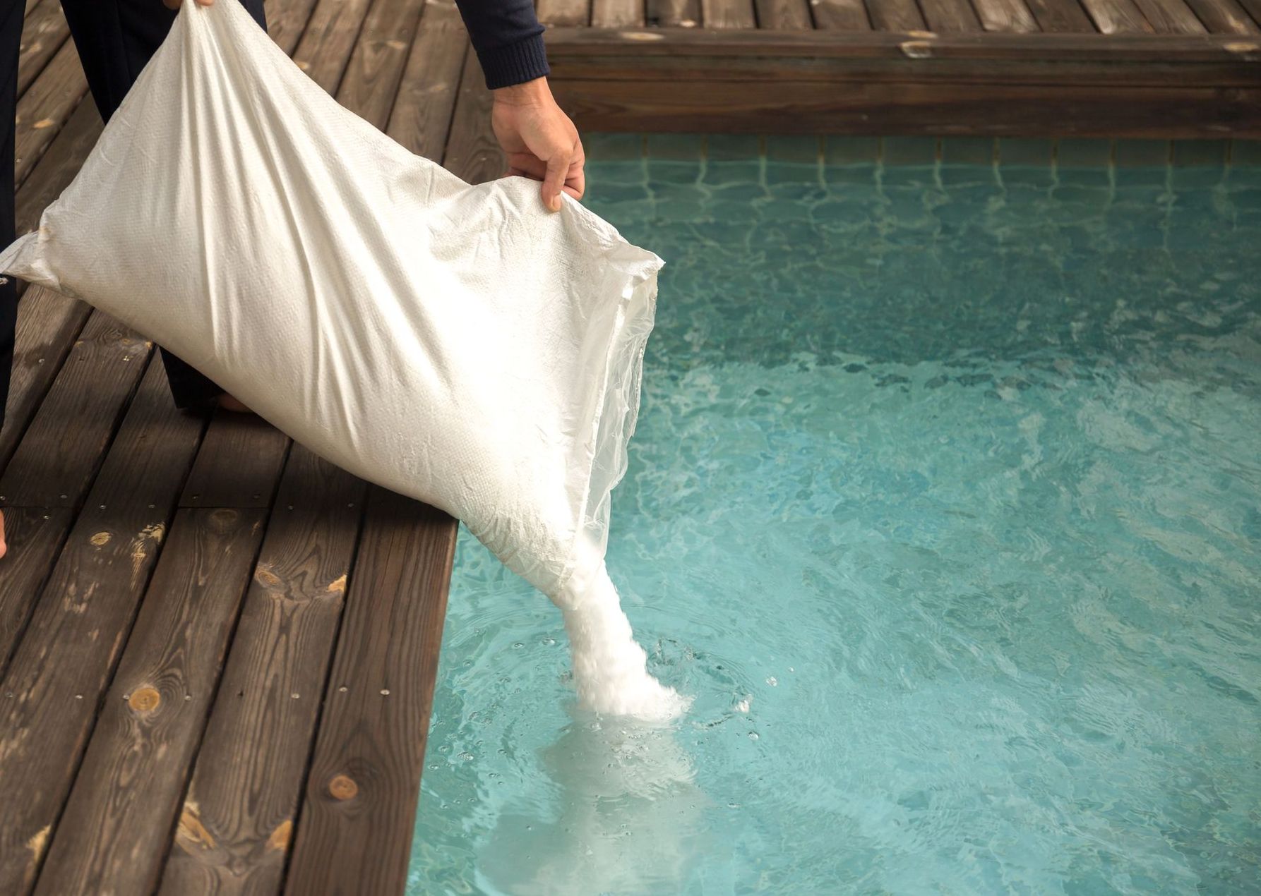 A person is carrying a bag of salt into a swimming pool.