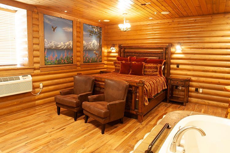 A bedroom in a log cabin with a bed , chairs , and a tub.