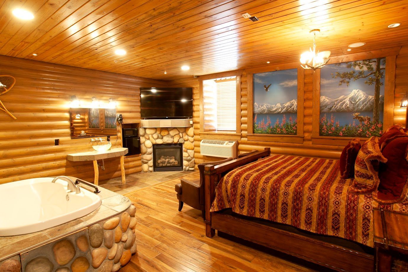 A bedroom in a log cabin with a bed , jacuzzi , fireplace and television.