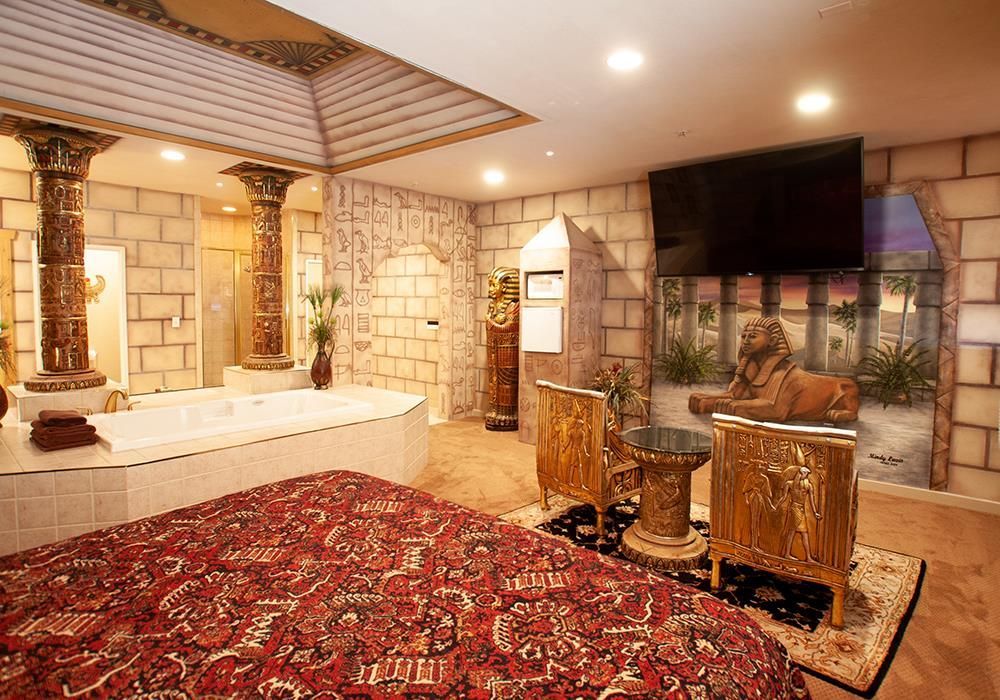 A bedroom with a large bed , chairs , a television and a bathtub.