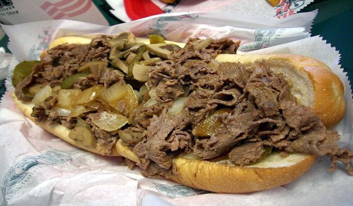 A steak sandwich with onions and pickles on a bun