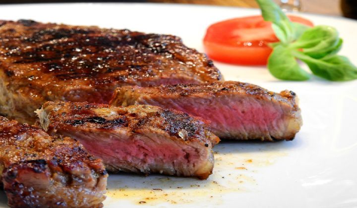 A close up of a steak on a plate with tomatoes and lettuce.