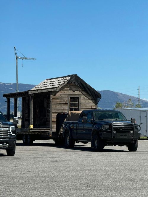A truck is pulling a small wooden house on a trailer