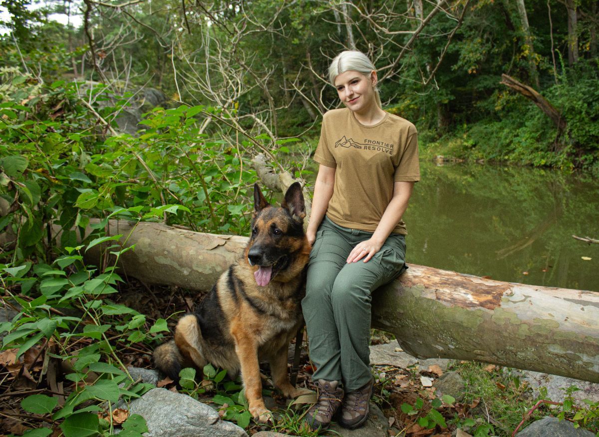 A woman is sitting on a log next to a german shepherd.