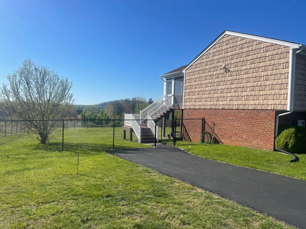 A house with stairs leading up to it is surrounded by grass and a chain link fence.