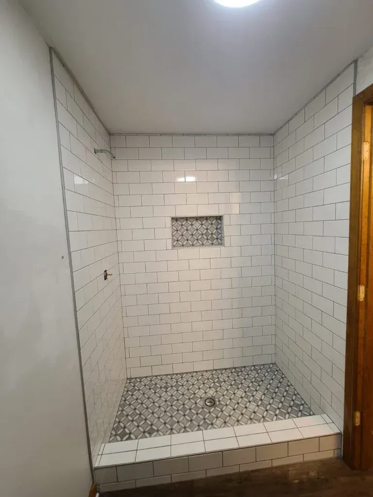 A bathroom with white tiles and a walk in shower.