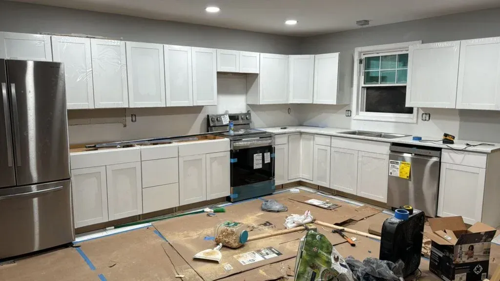 A kitchen under construction with white cabinets and stainless steel appliances.