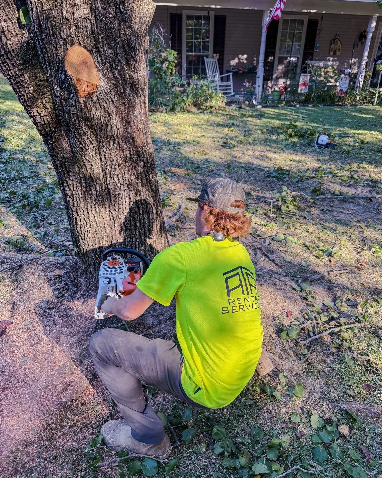 A man is cutting a tree with a chainsaw in front of a house.