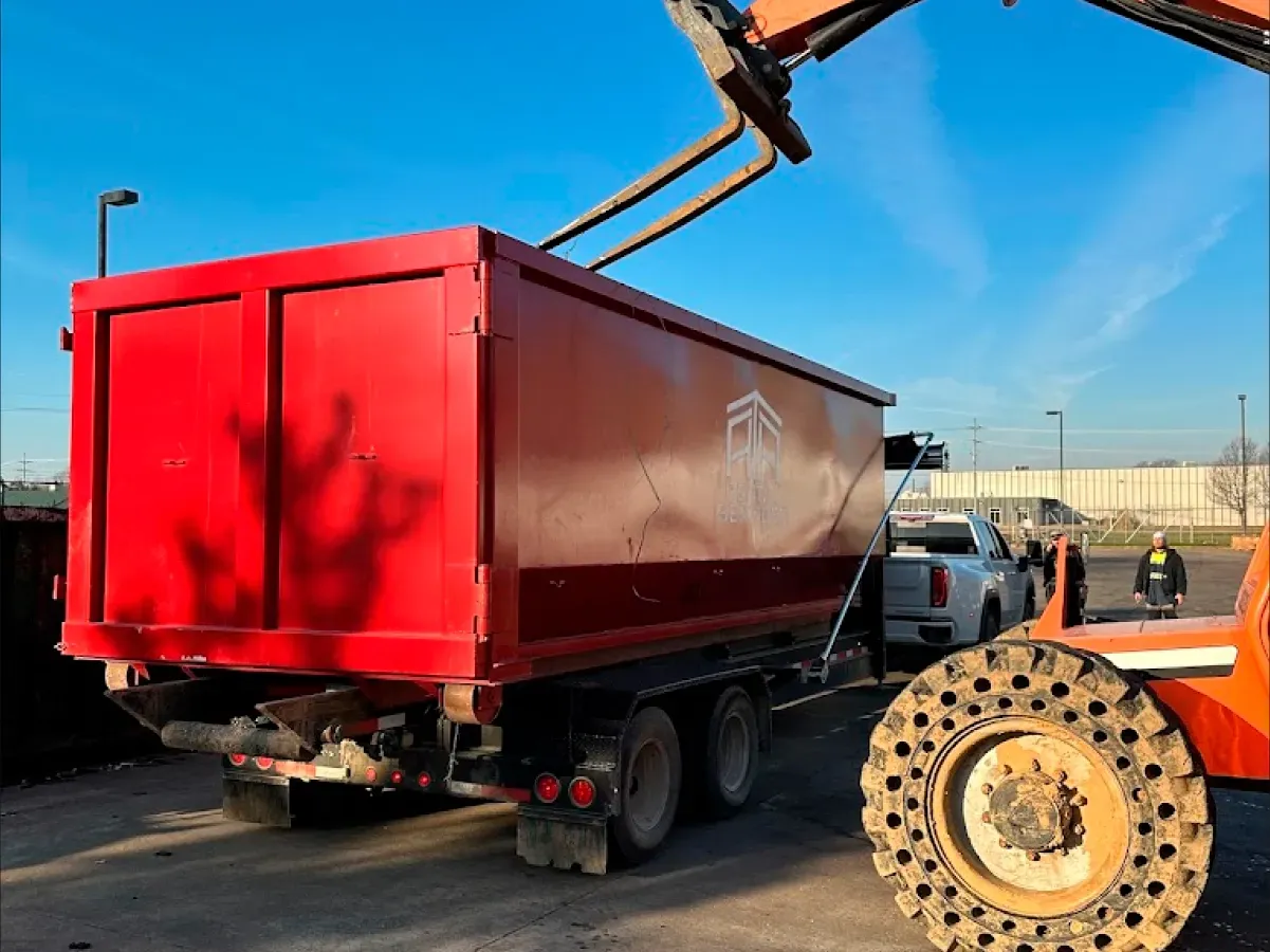 A red dump truck is being lifted by a crane in a parking lot.