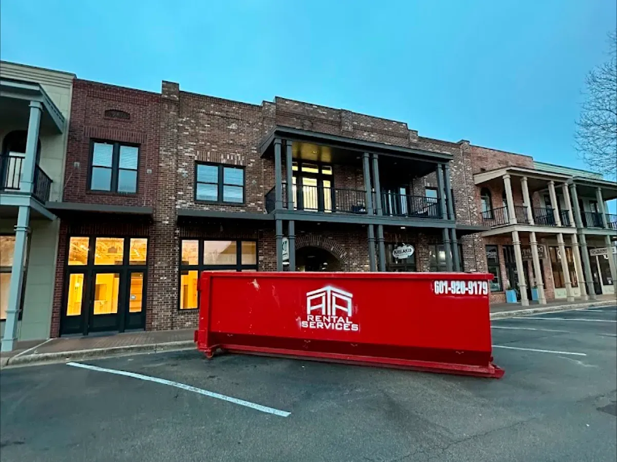 A large red dumpster is parked in front of a brick building.
