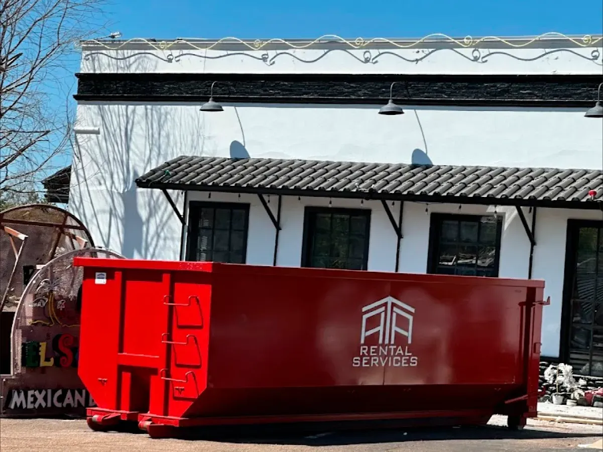A large red dumpster is parked in front of a white building.