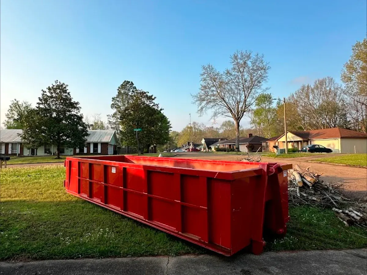 A large red dumpster is sitting in the grass in front of a house.