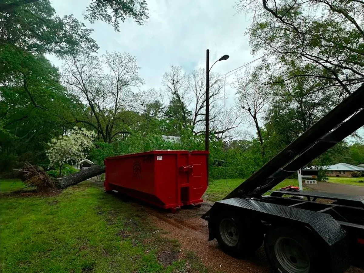 A red dumpster is sitting on the side of a road next to a dumpster trailer.
