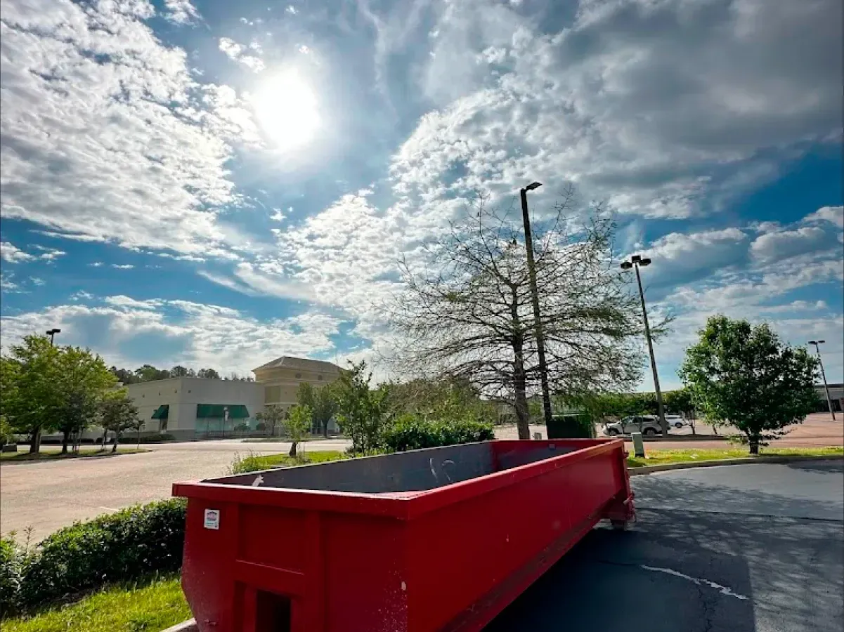 A red dumpster is parked in a parking lot in front of a building.