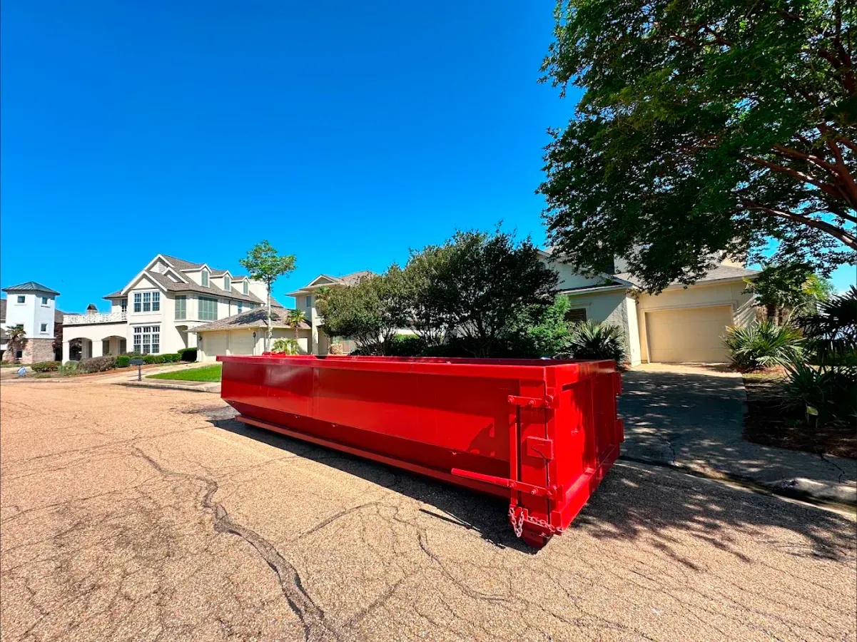 A large red dumpster is parked in front of a house.