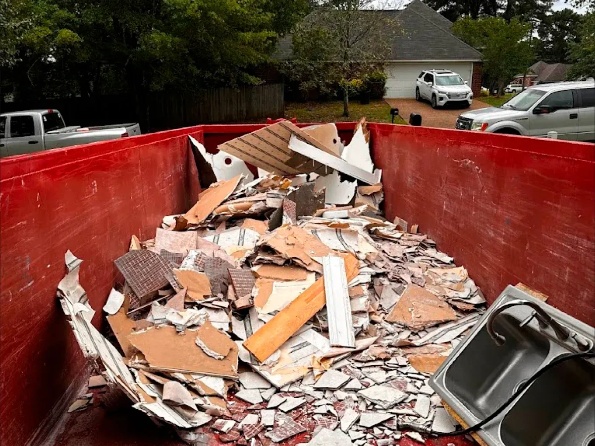 A red dumpster filled with a lot of junk in front of a house.