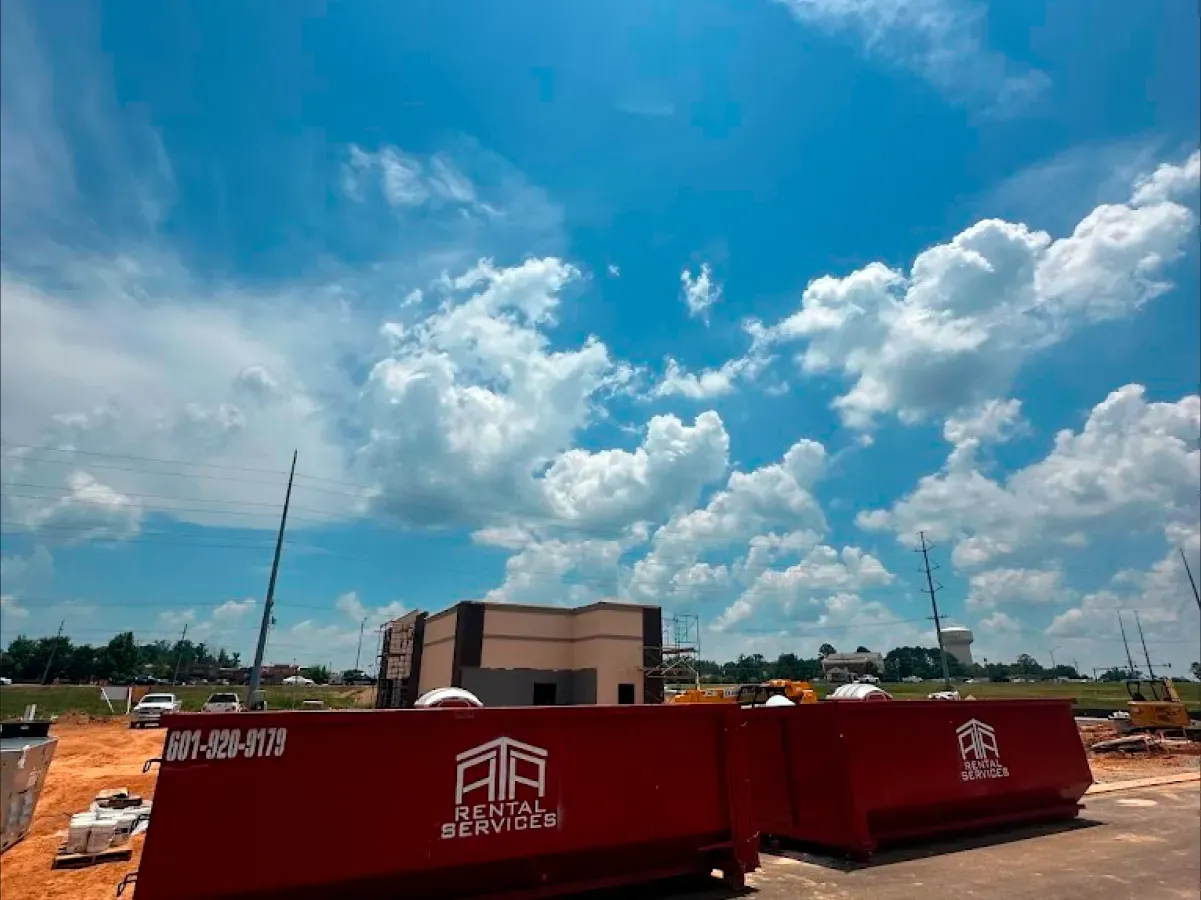 A red dumpster is parked in front of a building under construction.