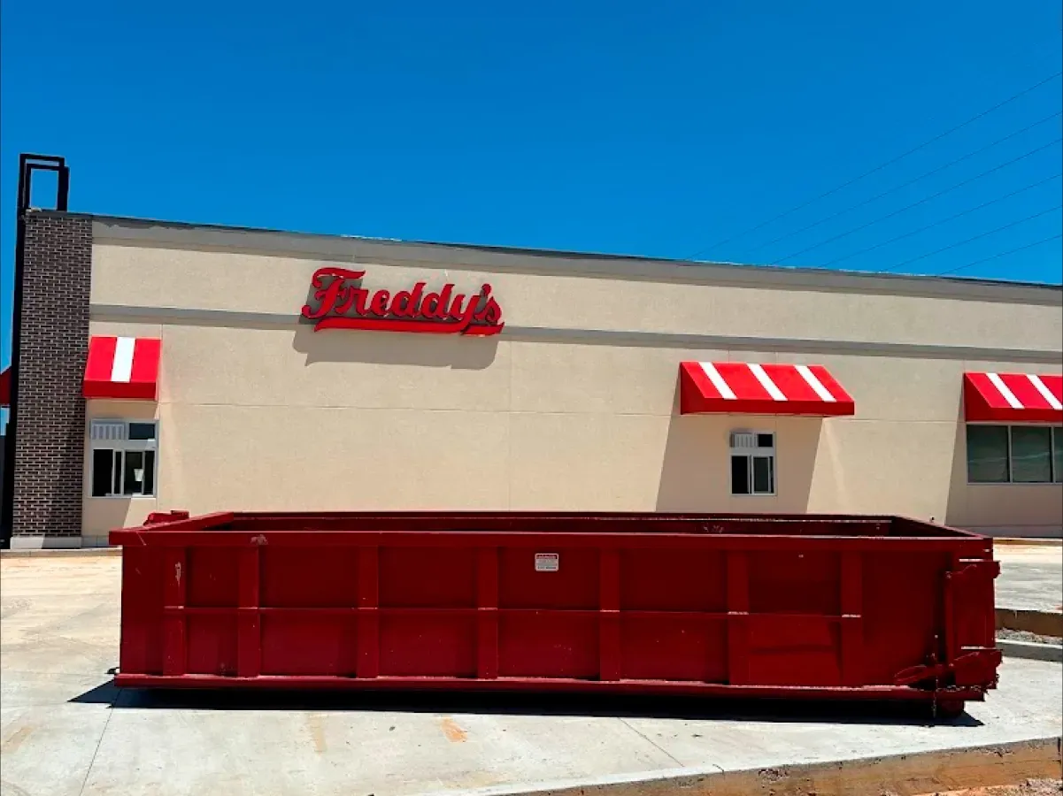A large red dumpster is parked in front of a franklin 's restaurant