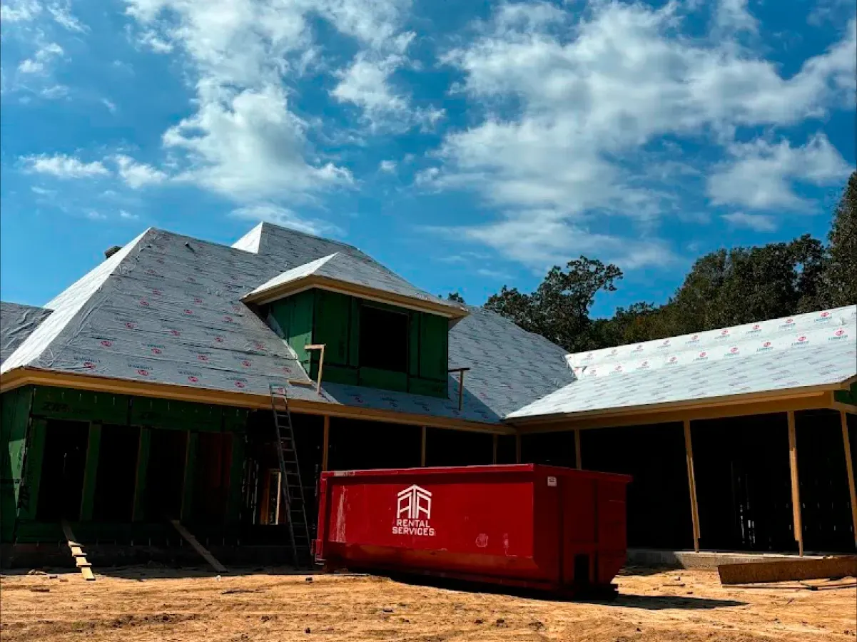 A large house under construction with a red dumpster in front of it.