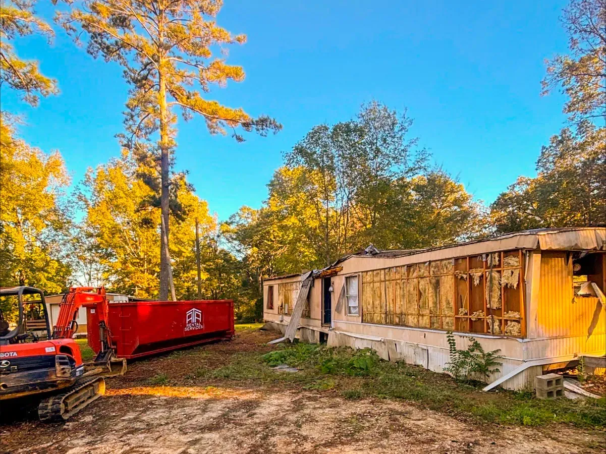 A red dumpster is sitting in front of a house that is being demolished.
