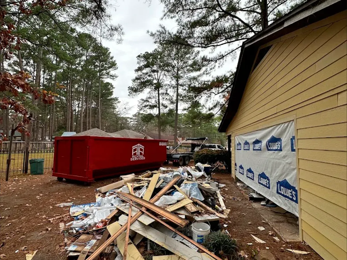 A pile of wood is sitting in front of a yellow house.